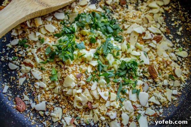 Toasted breadcrumbs, minced garlic, and sliced almonds in a pan, ready for butter and stirring.