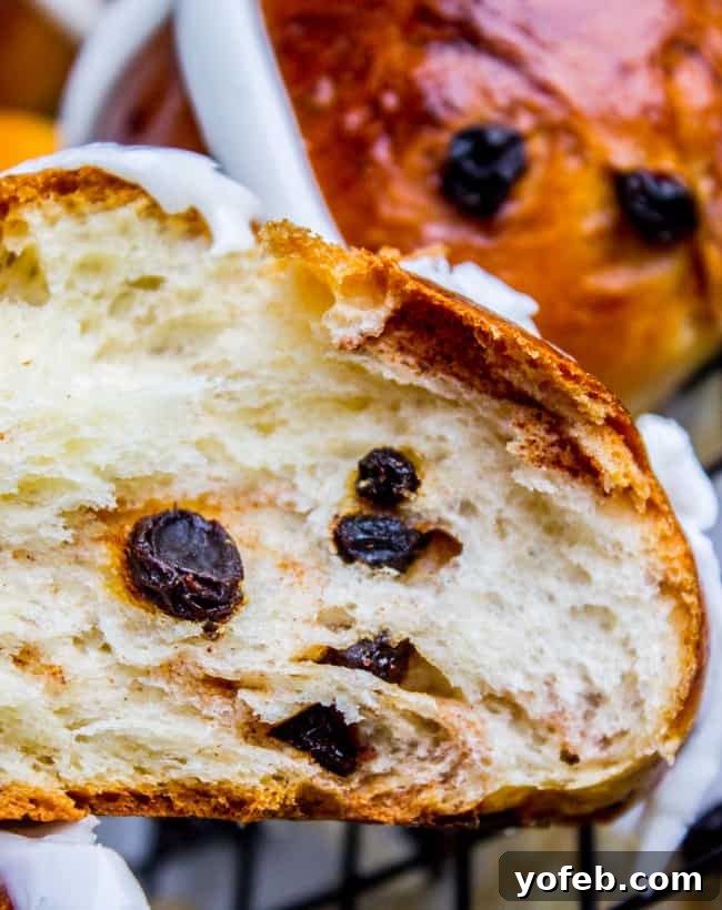 The Best Homemade Hot Cross Buns 4 A hot cross bun sliced in half, revealing the soft, fluffy interior with currants distributed throughout.