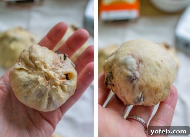 The Best Homemade Hot Cross Buns 8 A baker's hand holding a raw, shaped hot cross bun, showing the technique for forming a smooth ball.