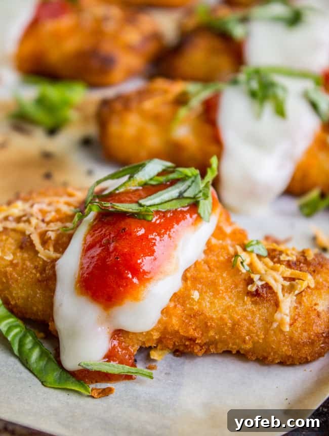 Crispy Fish Parmesan The Seafood Classic 4 A single crispy fish stick, beautifully plated and topped with a slice of fresh mozzarella, a dollop of rich tomato sauce, and a sprig of vibrant basil on a clean white plate.