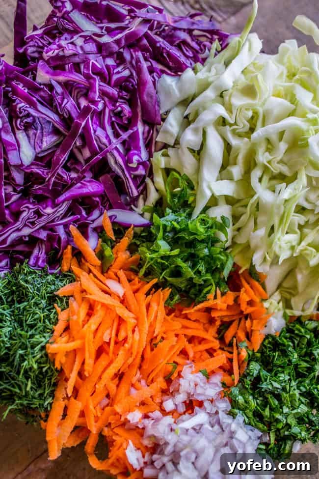 Zesty Lemon Herb Coleslaw 4 Close-up of thinly sliced green and red cabbage, and shredded carrots on a cutting board, prepared for making homemade coleslaw.