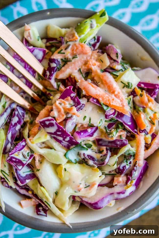 Zesty Lemon Herb Coleslaw 5 A fork dipping into a generous bowl of homemade lemon herb coleslaw, highlighting its creamy texture and fresh ingredients.