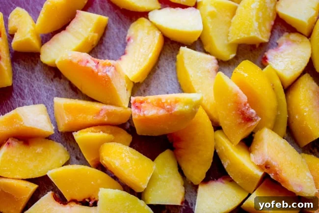 Velvet Peach Brown Sugar Dream 6 Close-up of frozen peach slices being cut in half on a wooden cutting board, preparing them for the cake batter.