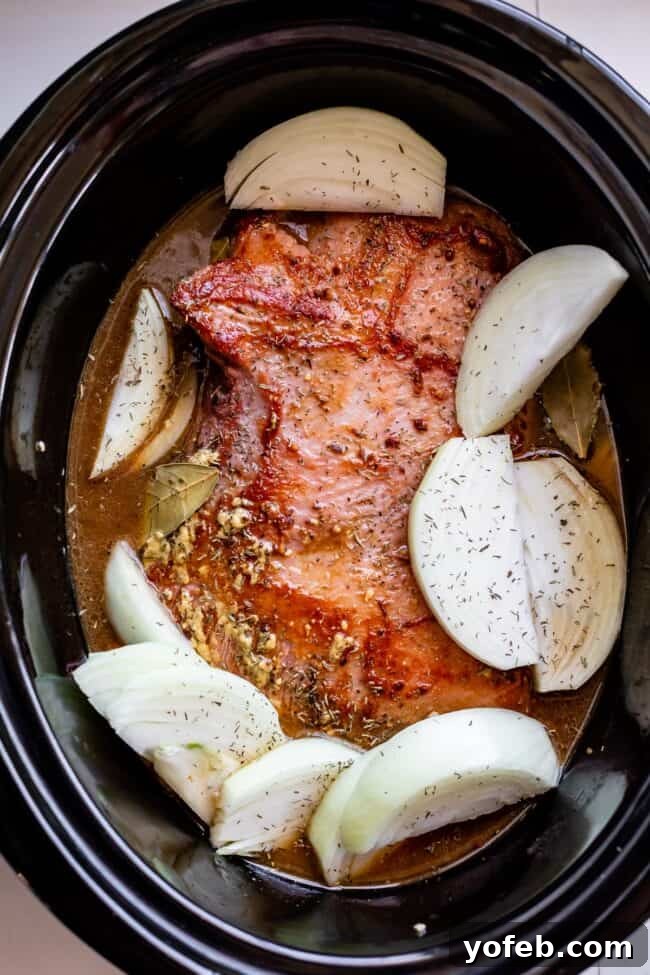 Ultimate Corned Beef Slow Cooker or Oven 14 Seared corned beef brisket nestled among onion wedges in a slow cooker, bubbling gently with aromatic liquids, signaling hours of tender cooking ahead.