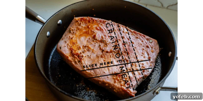 Ultimate Corned Beef Slow Cooker or Oven 18 A close-up of raw corned beef brisket being seared in a pan, with illustrative arrows showing the correct direction to slice against the grain for maximum tenderness.