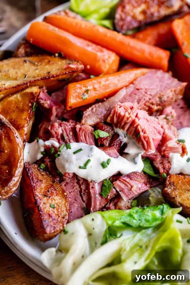 Ultimate Corned Beef Slow Cooker or Oven 7 A hearty portion of corned beef and cabbage, alongside roasted red potatoes and carrots, on a pristine white plate, embodying a classic comfort meal.