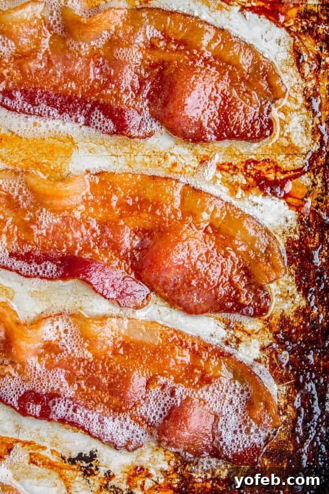 How to Bake Bacon in the Oven in 12 Minutes from the Food Charlatan. I literally never make bacon on the stove anymore. It is SO much easier cooking bacon in the oven than to stand over a hot stove getting splattered with grease. And you can make a whole pan at a time, making it great for a crowd. You can even make it ahead! Let me show you how to bake bacon - it's simple. #bakingbacon #bacon #intheoven #howto #crispy #breakfast #simplerecipe #cookiesheets #350 #lowcarb #comfortfoods A close-up view of perfectly crispy bacon, hot and ready on a sheet pan, showing its golden-brown texture.