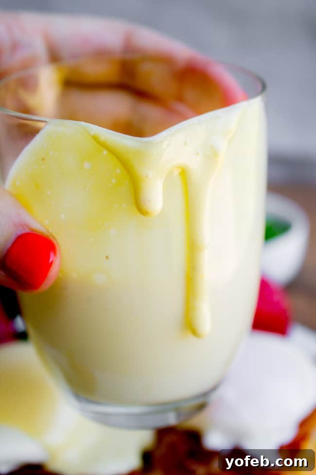 Blender Hollandaise Sauce Recipe (5 Minute Recipe) from The Food Charlatan: A vibrant, creamy hollandaise sauce in a white serving dish, garnished with fresh herbs, ready to be enjoyed with breakfast or brunch.