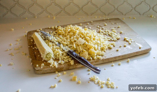 Mexican Street Corn Dip (Elote) from The Food Charlatan. This corn dip recipe is just like an elote (Mexican street corn). It is the perfect combo of sweet corn and savory tart cheese. Plus it's a lot easier to eat AND you get tortilla chips. Win! #corn #dip #elote #mexican #streetfood #summerfood #4thofjuly #cincodemayo #cotija #cornonthecob A close-up of a chef's knife expertly slicing kernels off a corn cob, a crucial step for the dip.
