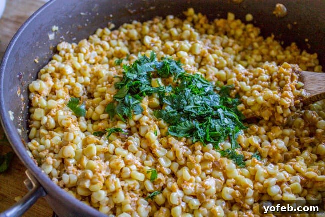 Mexican Street Corn Dip (Elote) from The Food Charlatan. This corn dip recipe is just like an an elote (Mexican street corn). It is the perfect combo of sweet corn and savory tart cheese. Plus it's a lot easier to eat AND you get tortilla chips. Win! #corn #dip #elote #mexican #streetfood #summerfood #4thofjuly #cincodemayo #cotija #cornonthecob Freshly chopped cilantro being added to a large bowl of Mexican Corn Dip, enhancing its color and aroma.