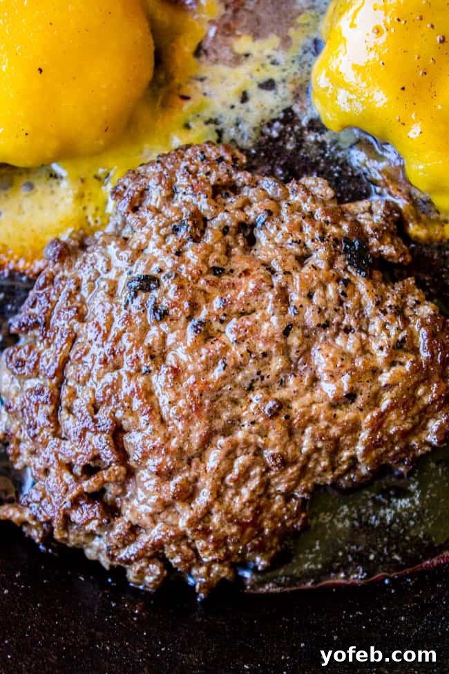Achieve the Perfect Melt: Best Smash Burger A close-up of a freshly made smash burger with gloriously melted cheese, with more burgers cooking in the background.