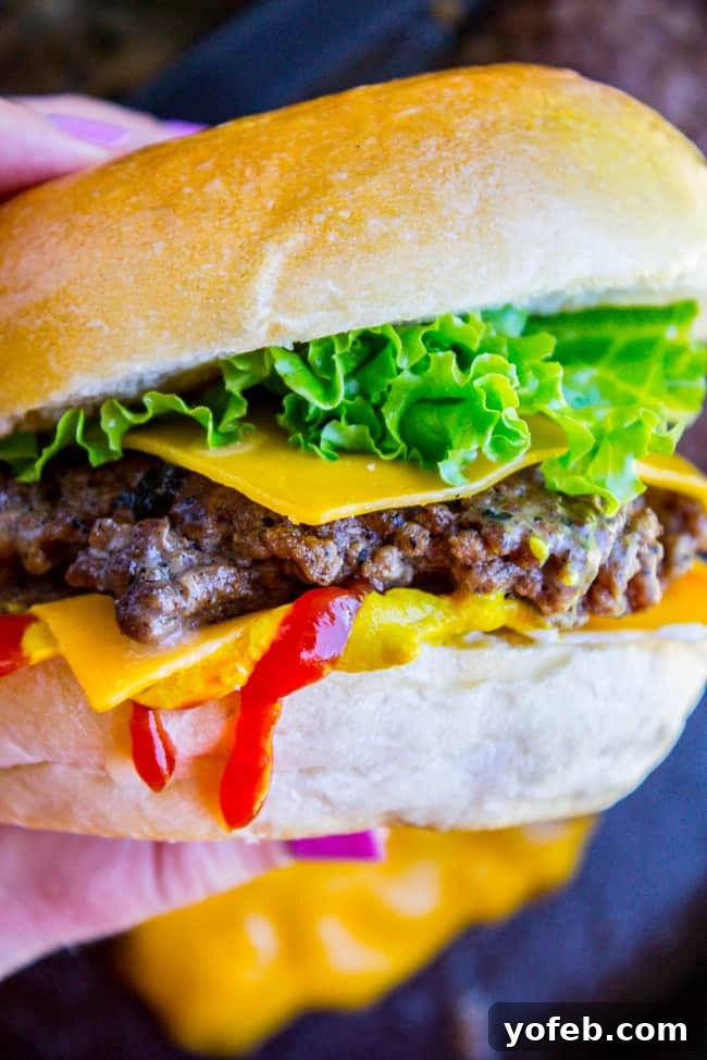 Handheld Perfection: Juicy Homemade Smash Burger A hand holds a delicious, juicy homemade smash burger, showcasing its perfect form and appetizing layers.