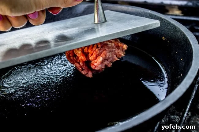 Smashing Beef onto a Hot Cast Iron Skillet A heavy grill press firmly smashing a ball of ground beef onto a hot cast iron skillet, creating a thin patty.