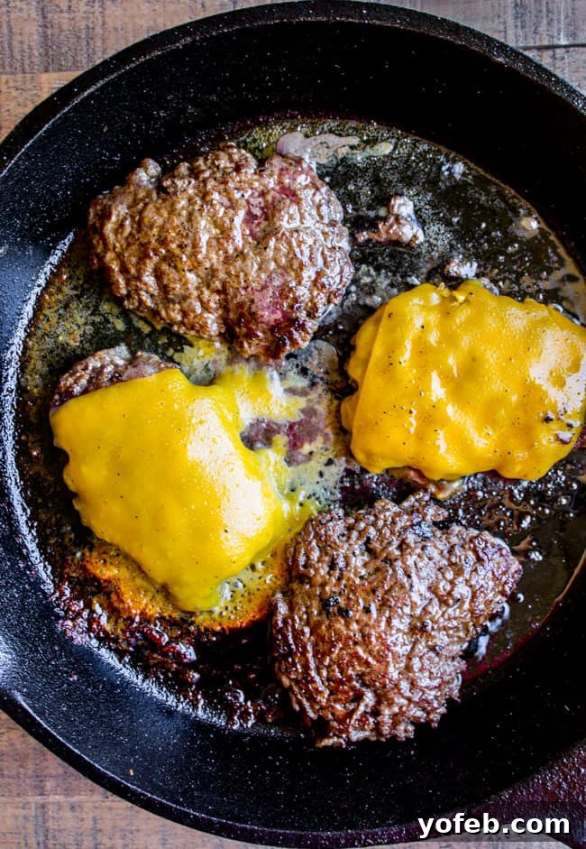 Smash Burgers with Melting Cheese in Cast Iron Juicy smash burgers, some topped with melted American cheese, cooking perfectly in a cast iron skillet.