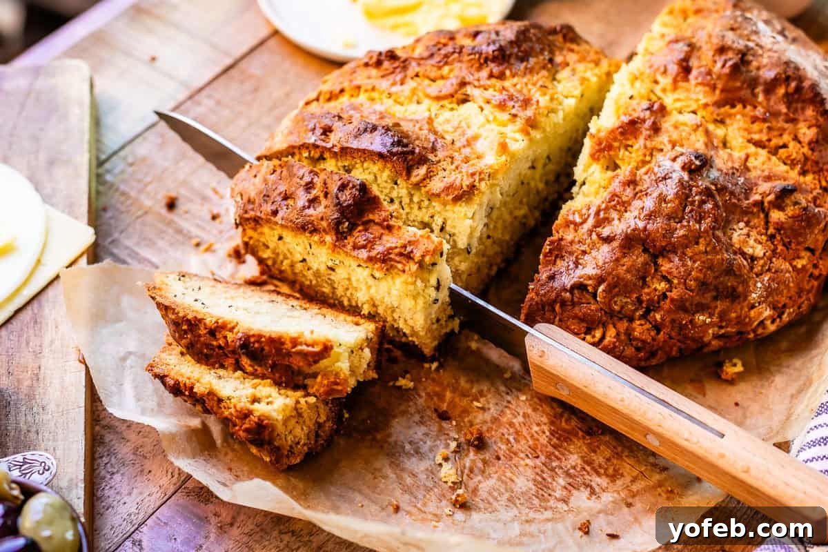 Pure Irish Soda Bread Perfection 17 Round loaf of Irish soda bread in halves being sliced with bread knife on parchment paper on top of wooden cutting board.
