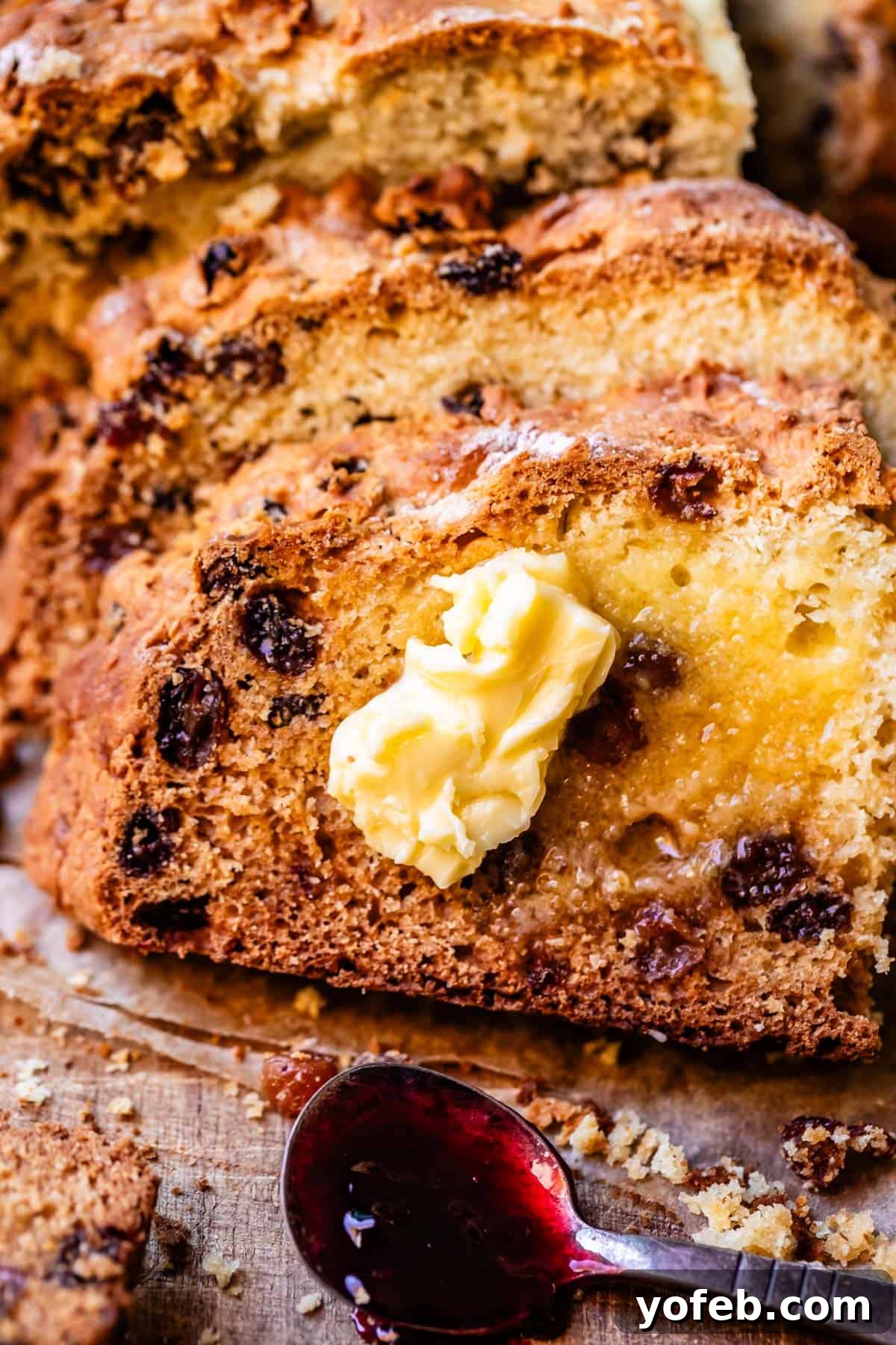 Pure Irish Soda Bread Perfection 6 Irish soda bread slices leaning atop one another on cutting board with pat of butter on top and small spoon with blackberry jam.