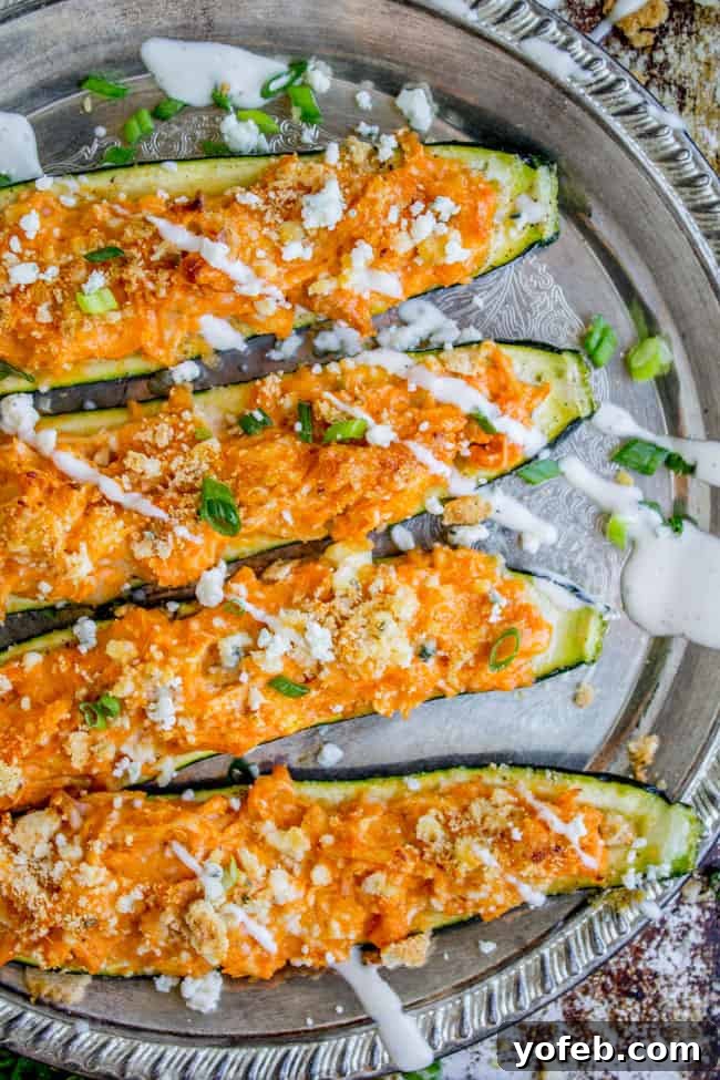 Fiery Buffalo Chicken Zucchini Boats 2 Buffalo Chicken Zucchini Boats topped with blue cheese and ranch dressing on a silver tray.