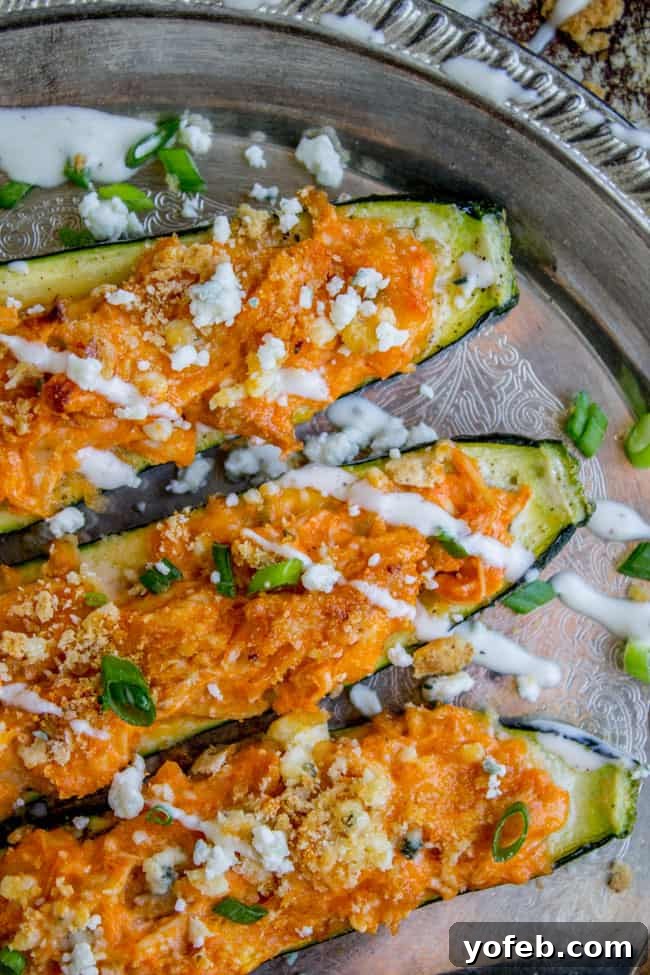 Fiery Buffalo Chicken Zucchini Boats 8 Buffalo Chicken Zucchini Boats topped with blue cheese and ranch dressing on a silver tray.
