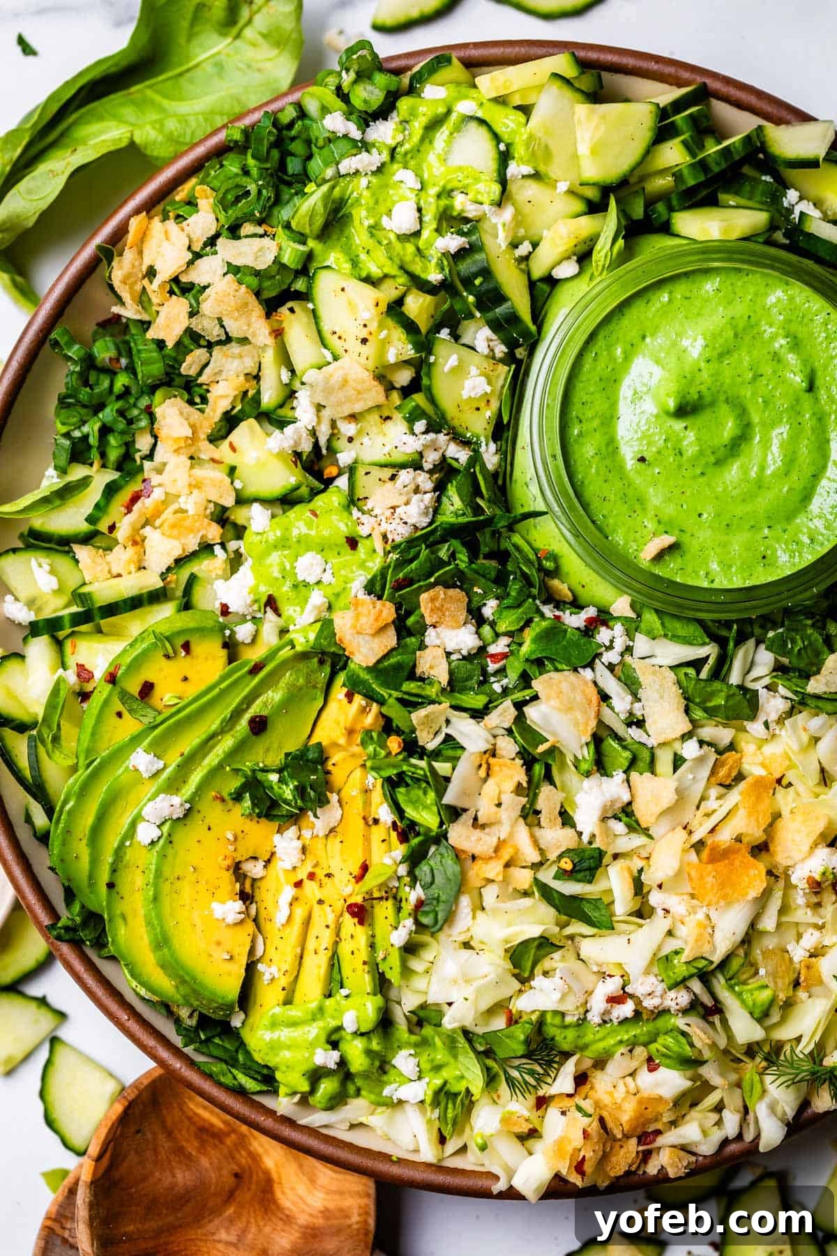 Effortless Feta and Beet Green Salad 9 plate full of green goddess salad topped with chips, avocado, and extra dressing.