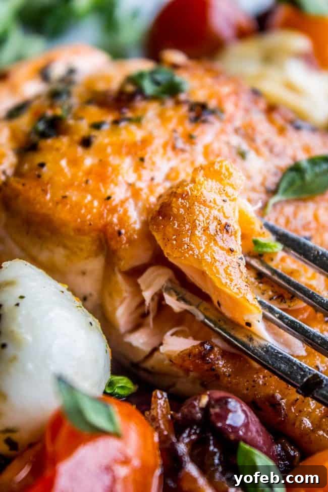 Speedy Pan-Seared Salmon with Burst Tomatoes and Melted Mozzarella 4 A fork lifts a flaky bite of pan-seared salmon, accompanied by a mozzarella ball and a cherry tomato, showcasing the dish's texture.