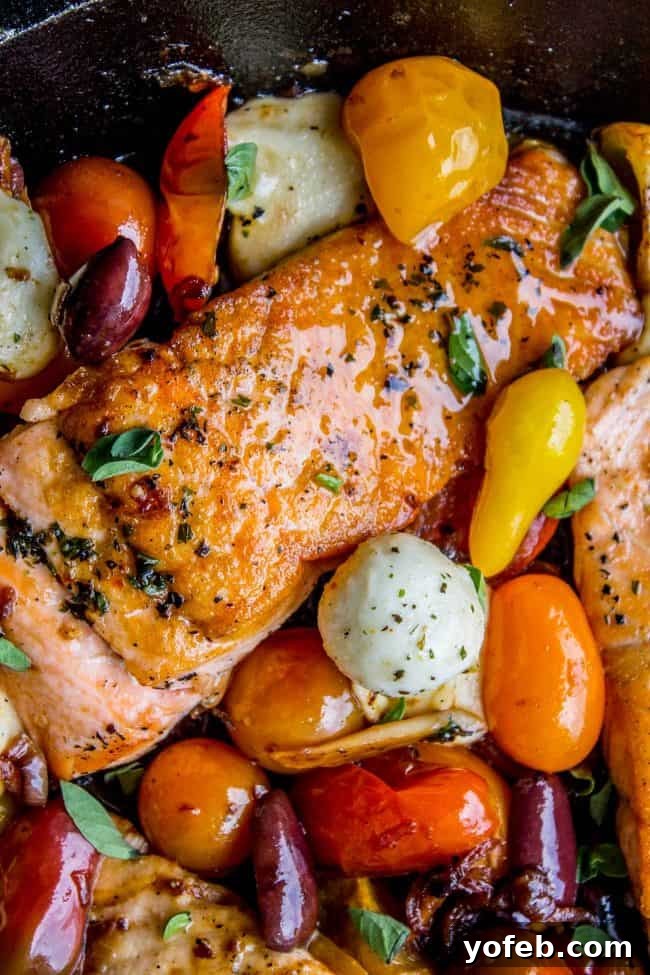 Speedy Pan-Seared Salmon with Burst Tomatoes and Melted Mozzarella 5 Cooked salmon fillet in a cast iron skillet, surrounded by vibrant cherry tomatoes, creamy mozzarella balls, and Kalamata olives.
