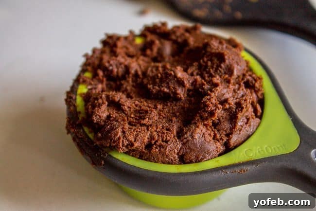 Decadent Double Chocolate Chip Cookies 10 A quarter cup measuring cup packed full of dark chocolate cookie dough, ready for shaping.