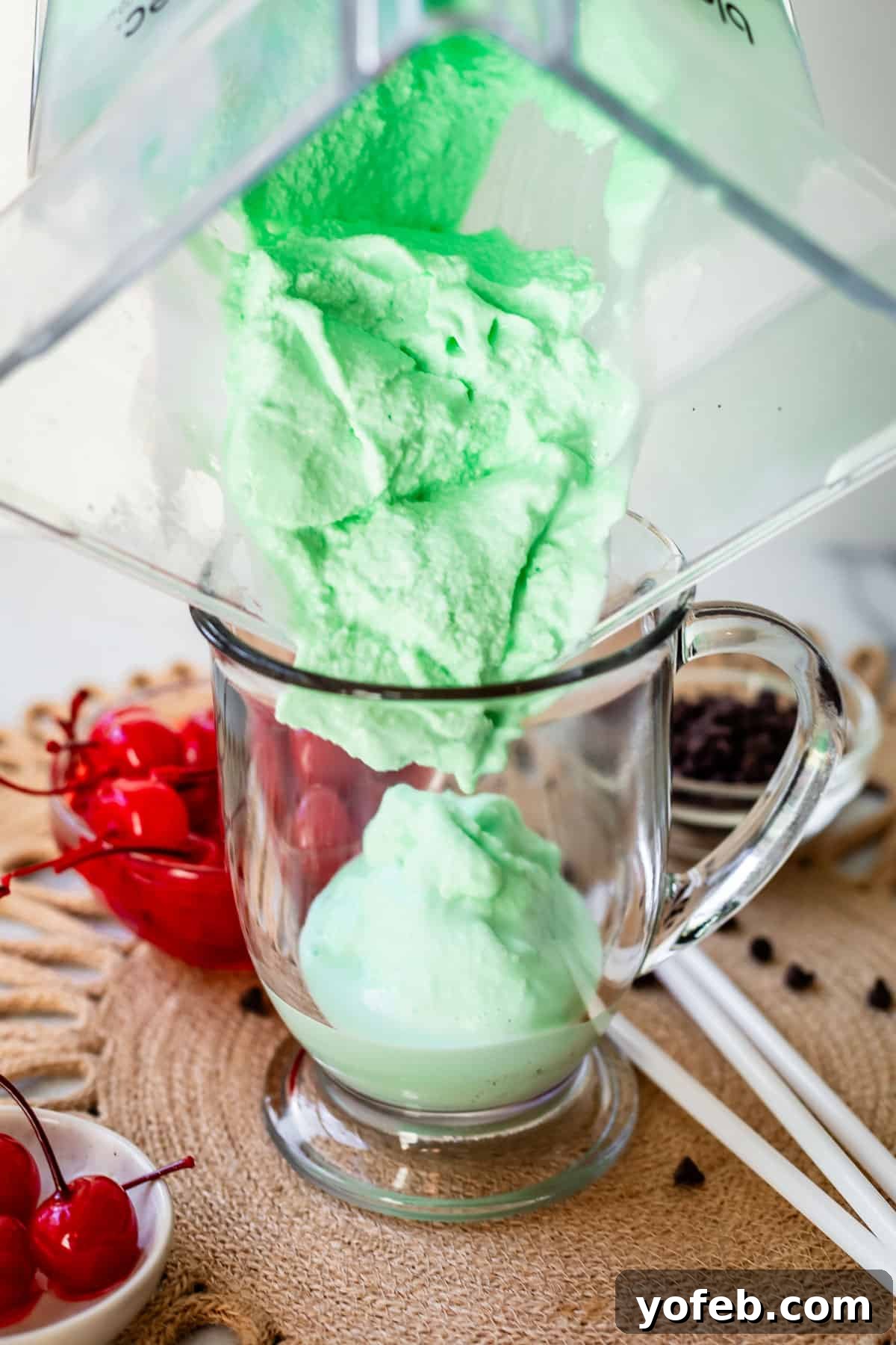Leprechaun's Delight Shake 13 A perfectly blended Shamrock Shake is being poured from a plastic blender pitcher into a clear glass mug with a handle, showing its creamy texture.