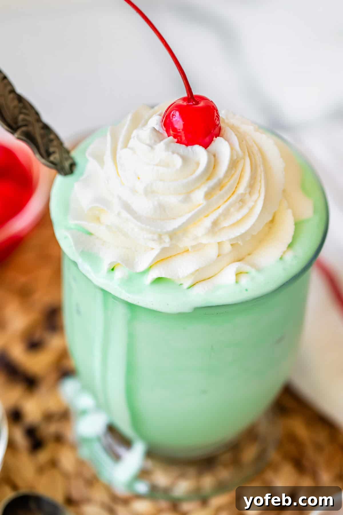 Leprechaun's Delight Shake 15 A glass filled with a bright green shake, beautifully topped with a swirl of piped whipped cream and a single maraschino cherry, perfectly ready to be enjoyed.
