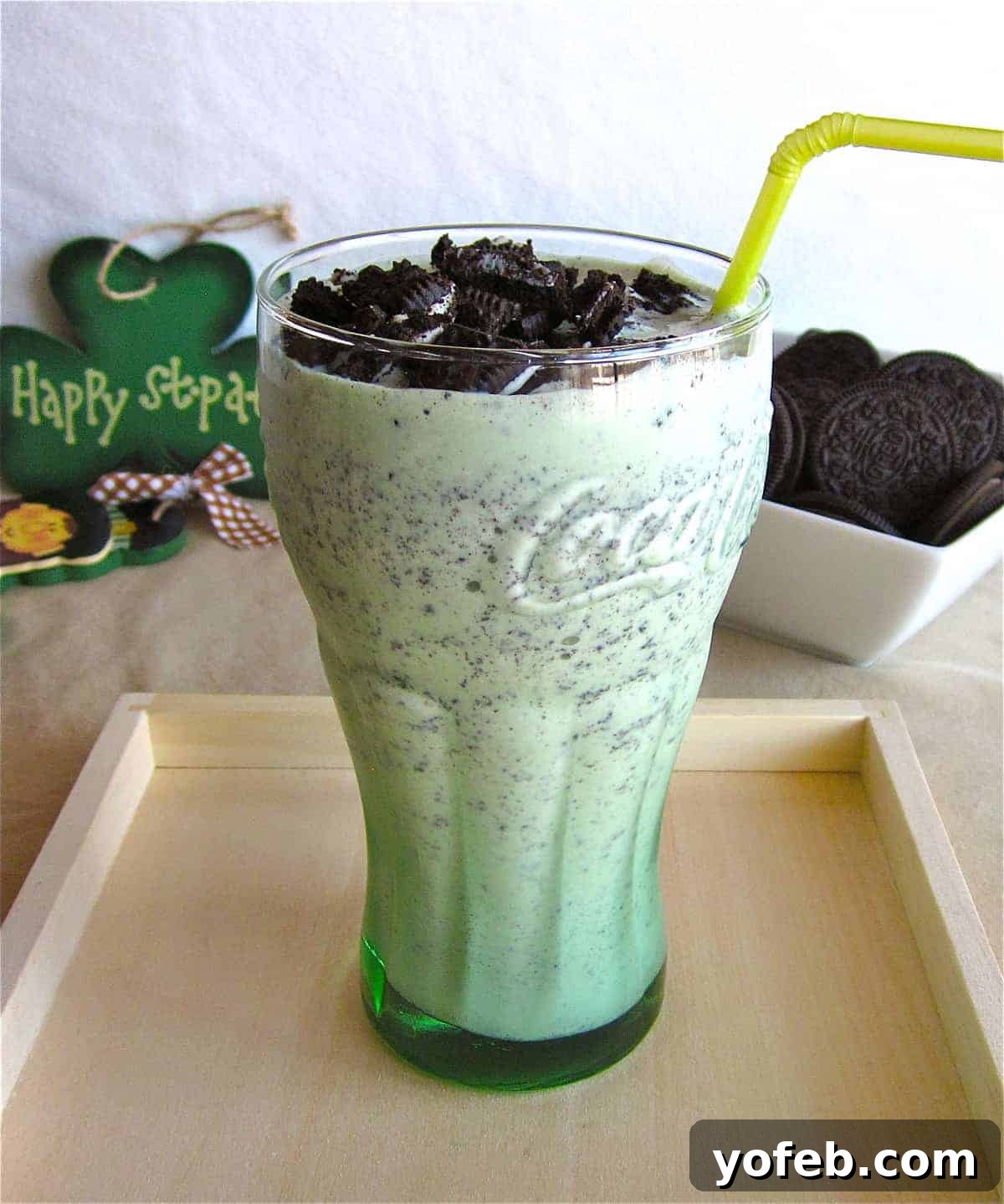 IMG_2527 An old blog photo of a Shamrock Shake in a clear glass, topped with whipped cream and crushed Oreos. A St. Patrick's Day wall hanging is visible in the background for decor.