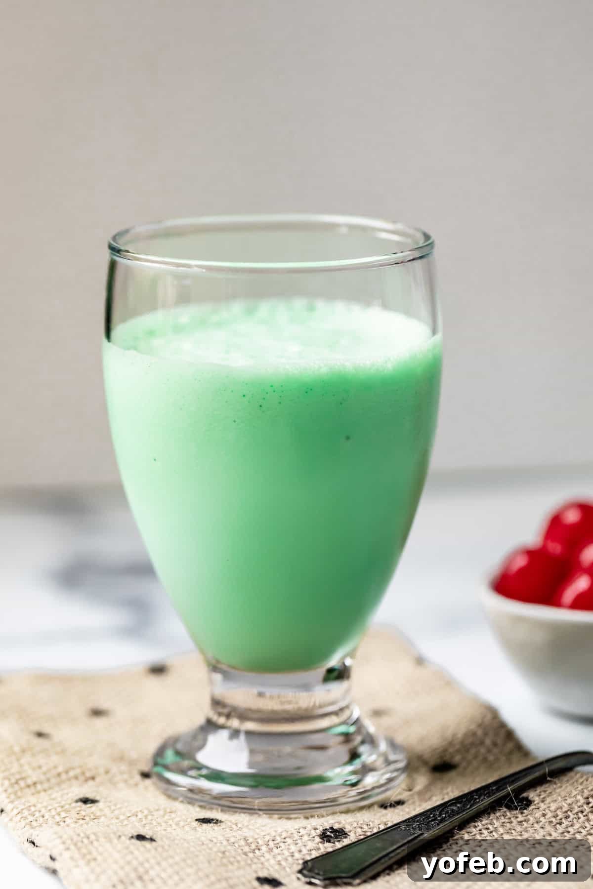 Leprechaun's Delight Shake 4 A simple, elegant glass on a cloth napkin, filled to the brim with a creamy, green Shamrock Shake. The setting suggests a relaxed, homemade enjoyment.