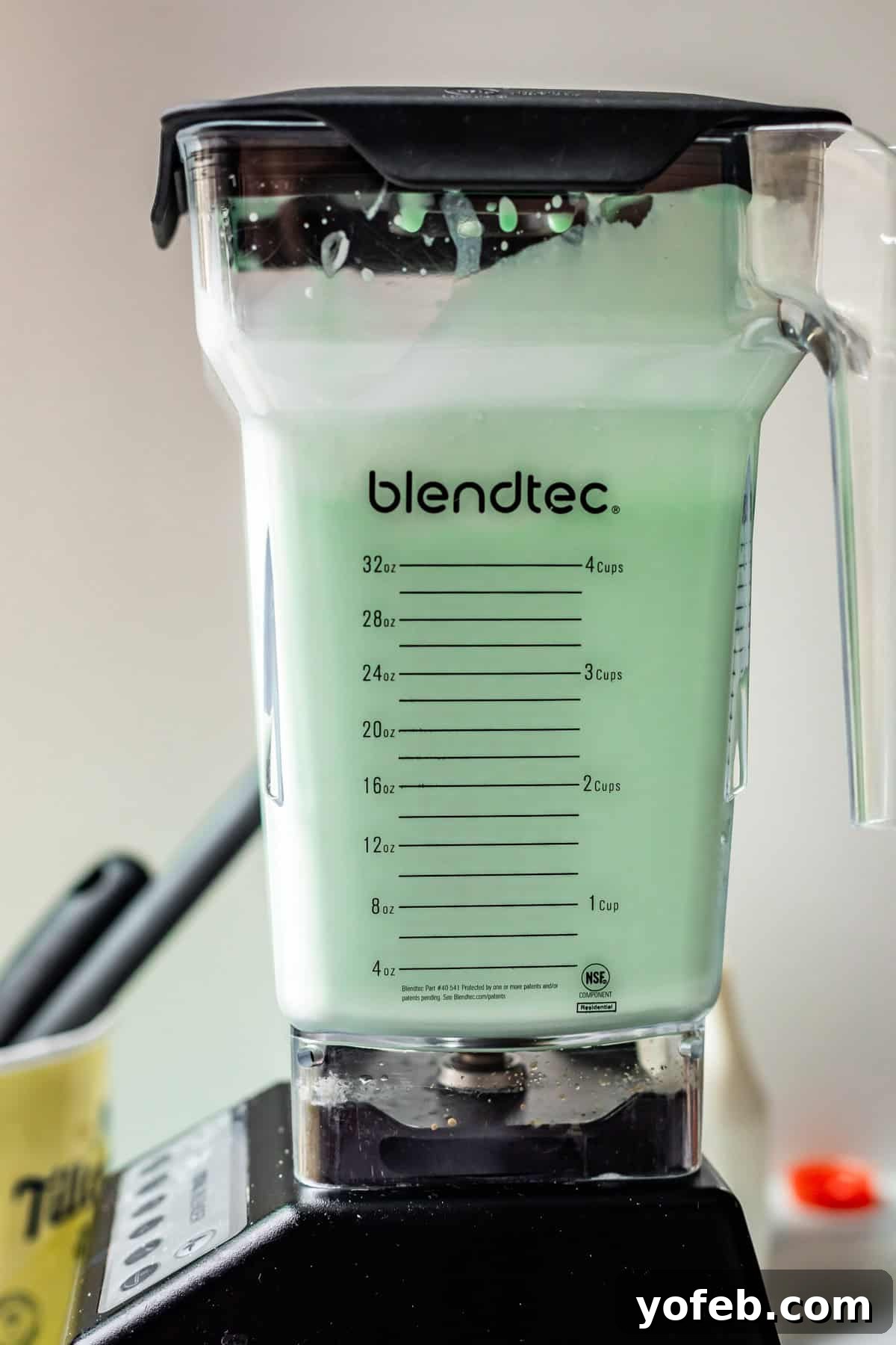 Leprechaun's Delight Shake 10 A Blendtec blender on its base, actively blending the Shamrock Shake ingredients into a smooth, green mixture. The consistency looks thick and creamy.