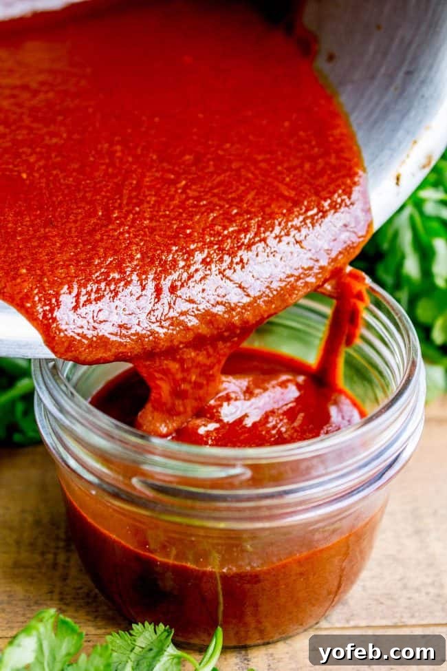 Speedy Homemade Enchilada Sauce 5 Homemade red enchilada sauce being poured into a clear glass mason jar for storage.