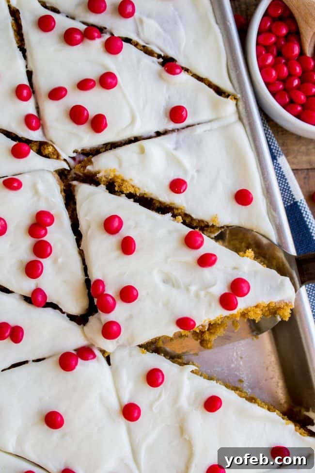 Decadent Pumpkin Squares with Cream Cheese Frosting 3 Pumpkin Bars with Cream Cheese Frosting and red hots in a sheet pan with a blue and white napkin, ready to be served.