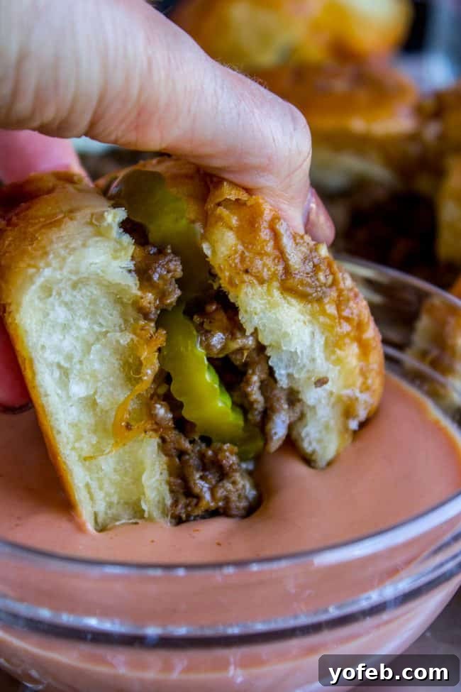 Irresistible Mini Burgers 8 Hand dipping a cheeseburger slider into a creamy sauce.