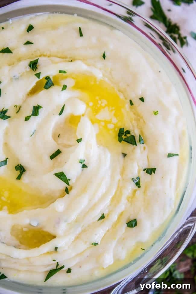 Creamy Mashed Potatoes: Aunt Shirley's Legendary Recipe - Fluffy, Creamy, Flavorful, Easy Homemade Side Dish for Thanksgiving, Pot Roast, or Any Meal. Made with Butter, Cream Cheese, and Garlic. A bowl of creamy mashed potatoes garnished with melted butter and fresh parsley.