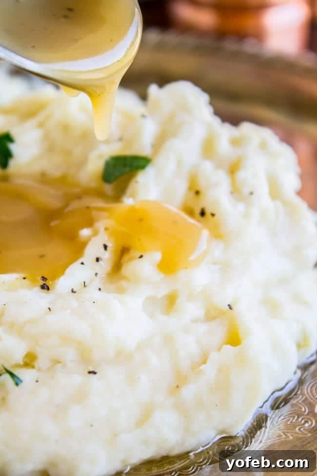 Creamy Mashed Potatoes: Aunt Shirley's Legendary Recipe - Fluffy, Creamy, Flavorful, Easy Homemade Side Dish for Thanksgiving, Pot Roast, or Any Meal. Made with Butter, Cream Cheese, and Garlic. Close-up of fluffy mashed potatoes with rich gravy being drizzled over them.