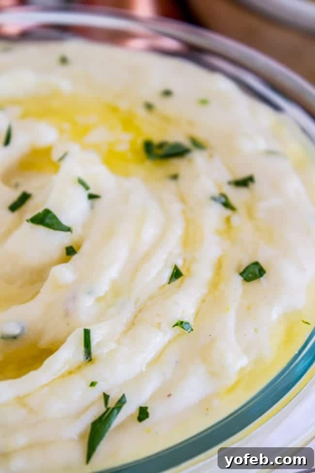 Creamy Mashed Potatoes: Aunt Shirley's Legendary Recipe - Fluffy, Creamy, Flavorful, Easy Homemade Side Dish for Thanksgiving, Pot Roast, or Any Meal. Made with Butter, Cream Cheese, and Garlic. A glass bowl overflowing with creamy mashed potatoes, adorned with melted butter and a sprinkle of fresh parsley.