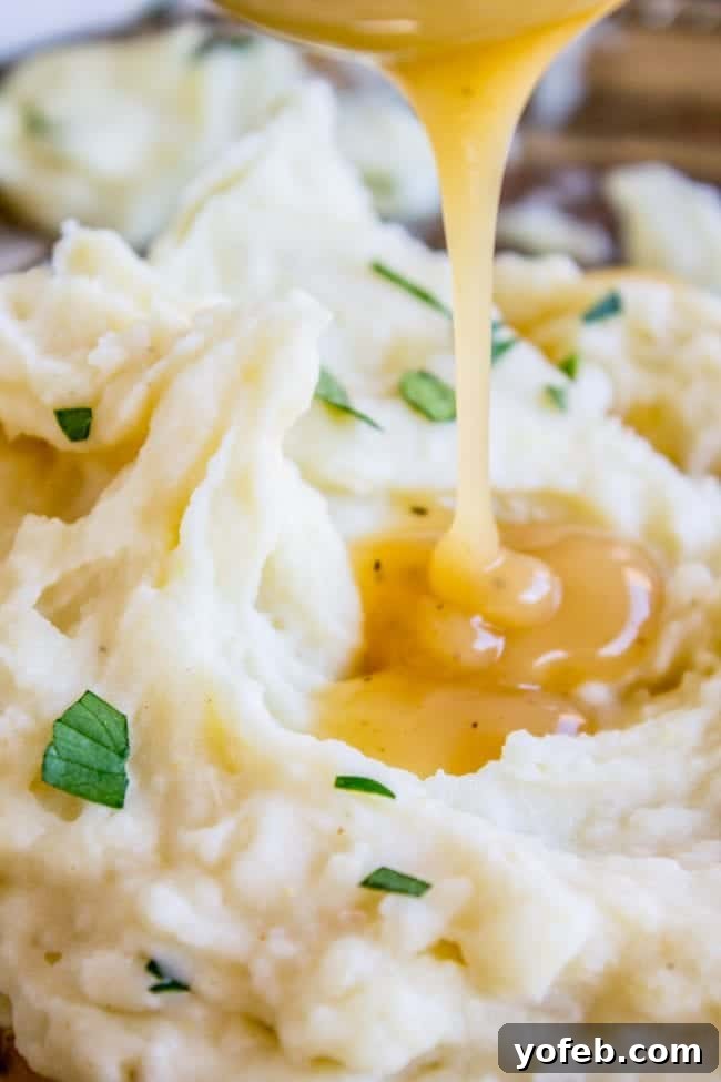 Creamy Mashed Potatoes: Aunt Shirley's Legendary Recipe - Fluffy, Creamy, Flavorful, Easy Homemade Side Dish for Thanksgiving, Pot Roast, or Any Meal. Made with Butter, Cream Cheese, and Garlic. A close-up shot of rich, savory gravy being poured over a generous serving of creamy mashed potatoes.
