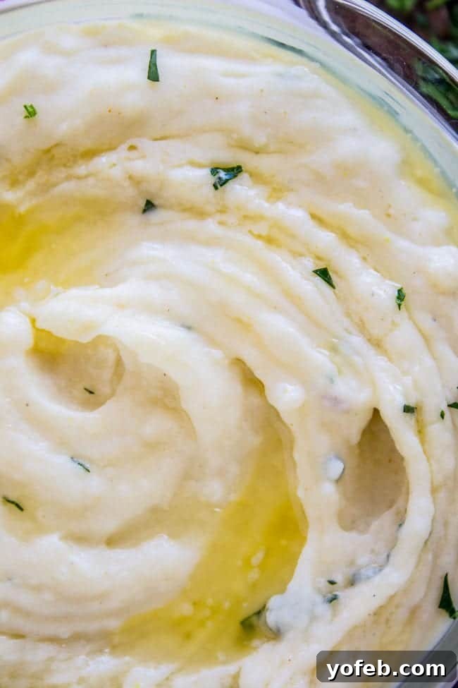 Creamy Mashed Potatoes: Aunt Shirley's Legendary Recipe - Fluffy, Creamy, Flavorful, Easy Homemade Side Dish for Thanksgiving, Pot Roast, or Any Meal. Made with Butter, Cream Cheese, and Garlic. A beautiful glass serving bowl filled with creamy mashed potatoes, topped with melted butter and fresh green parsley.