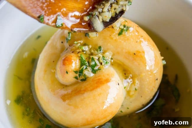 Dunking golden garlic knots in rich, herbaceous garlic butter for maximum flavor. Freshly baked garlic knots being generously drizzled and soaked in warm garlic parsley butter.