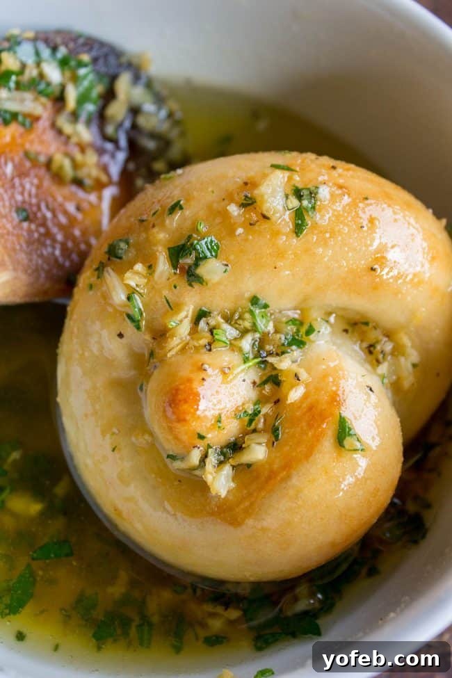 Garlic knots being infused with rich garlic butter, ready to serve warm. Freshly baked garlic knots soaking in a bowl of aromatic garlic parsley butter.