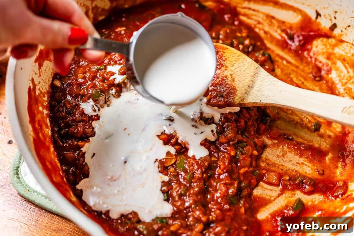 Chicken Tikka Masala A Culinary Revelation 12 hand pouring cream from a measuring cup into a pan with sauce.