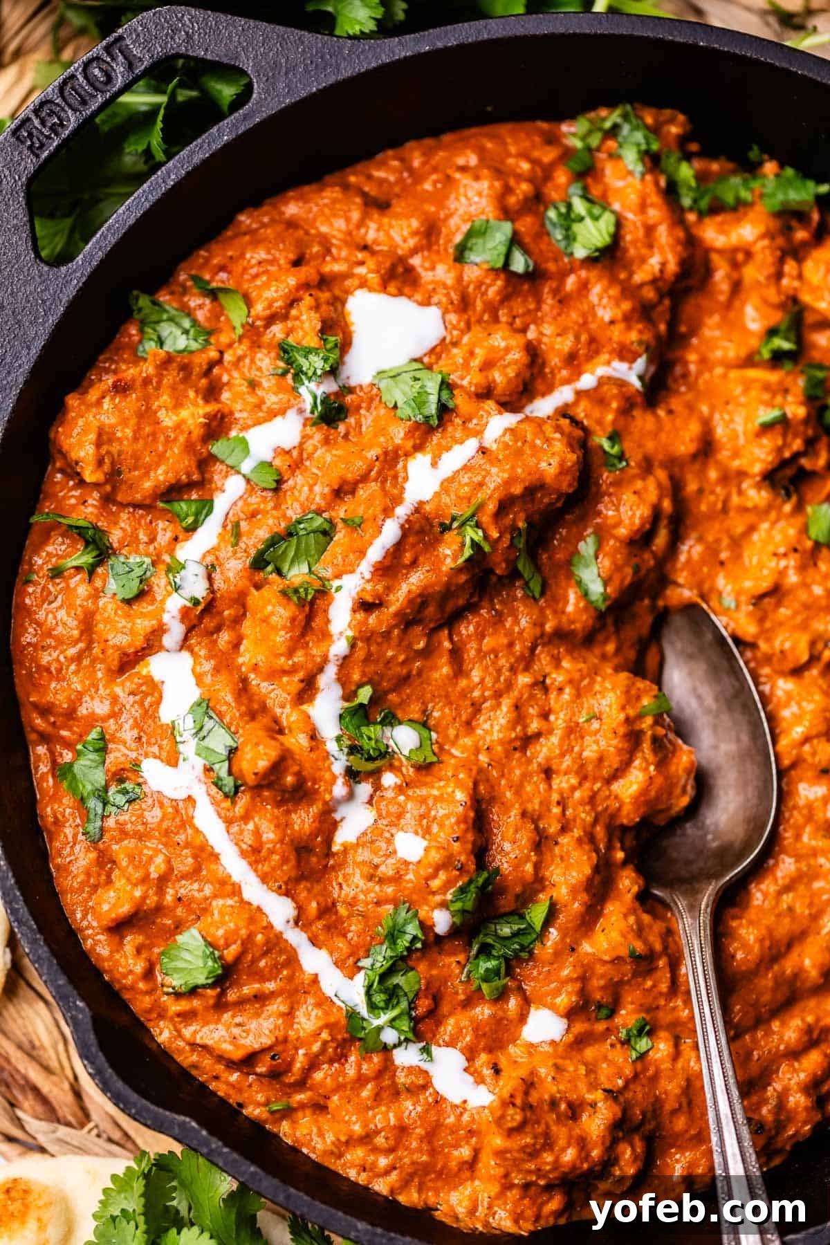 Chicken Tikka Masala A Culinary Revelation 19 cast iron skillet filled with tikka masala, garnished with cream and parsley, with a spoon in it.
