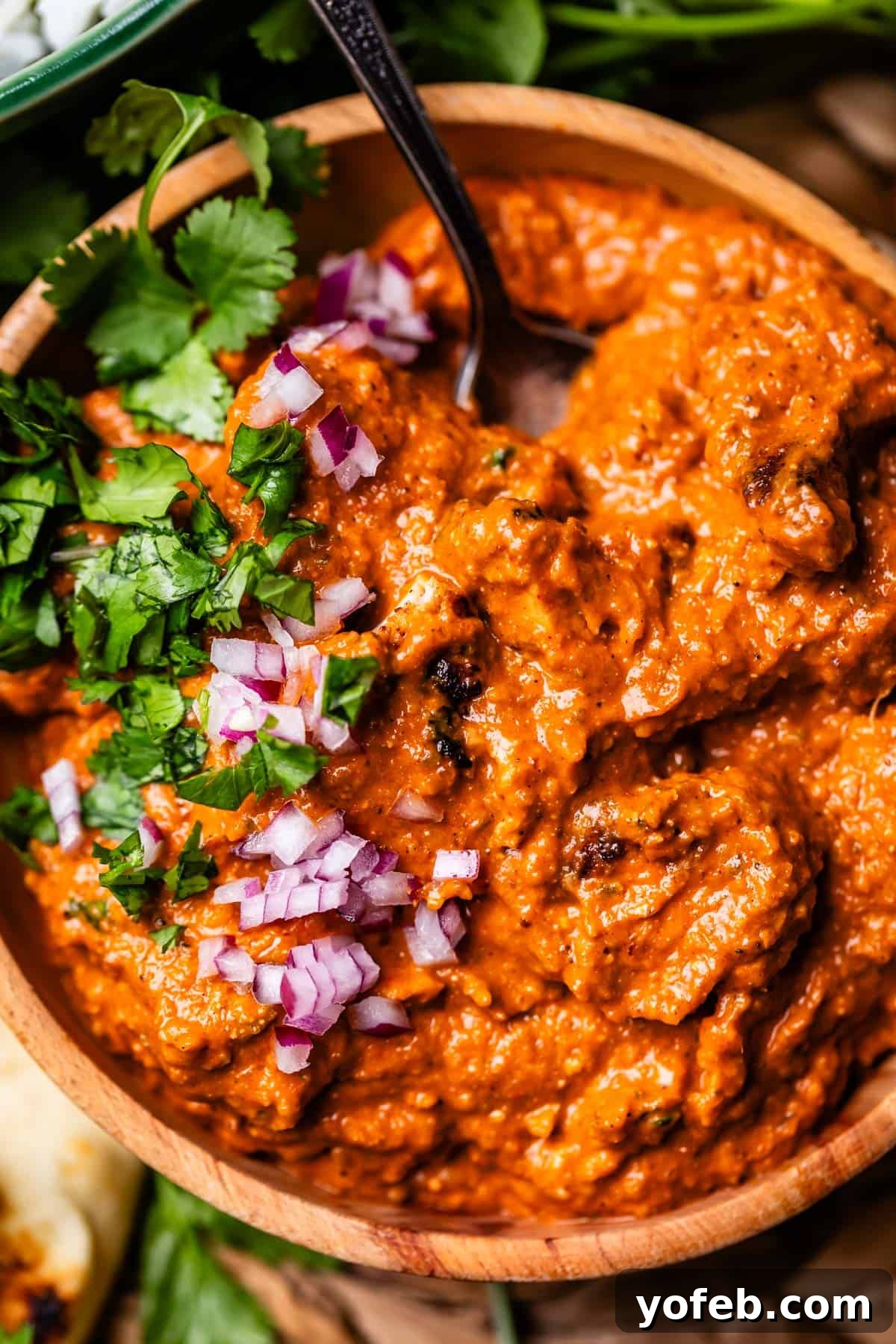 Chicken Tikka Masala A Culinary Revelation 20 wooden bowl filled with chicken tikka masala with red onion and cilantro garnish.