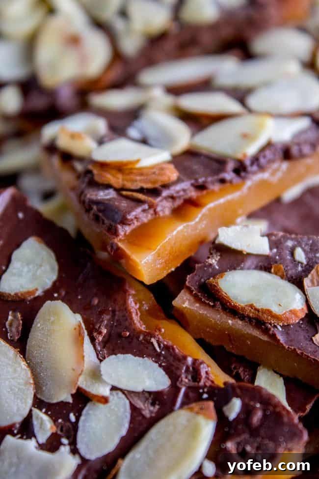 The Best Homemade English Toffee Recipe by The Food Charlatan. This is the BEST homemade English Toffee Recipe, hands down! This is such an easy and QUICK treat to make for the Christmas holidays. You don't even need a candy thermometer! #toffee #English #candy #Christmas #easy #homemade #tutorial #recipe #almonds A close-up of a stack of English toffee pieces, generously covered with chocolate and sliced almonds, inviting a bite.