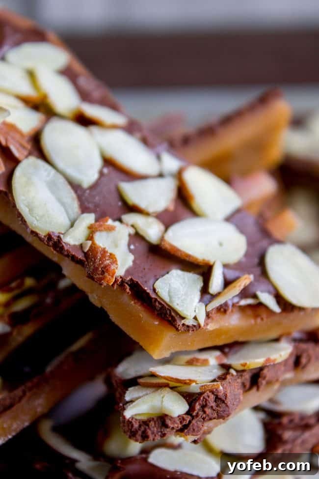 The Best Homemade English Toffee Recipe by The Food Charlatan. This is the BEST homemade English Toffee Recipe, hands down! This is such an easy and QUICK treat to make for the Christmas holidays. You don't even need a candy thermometer! #toffee #English #candy #Christmas #easy #homemade #tutorial #recipe #almonds English toffee close-up, generously covered in sliced almonds, with other pieces stacked askew, showcasing the tempting texture.