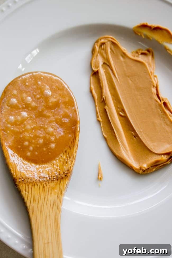 The Best Homemade English Toffee Recipe by The Food Charlatan. This is the BEST homemade English Toffee Recipe, hands down! This is such an easy and QUICK treat to make for the Christmas holidays. You don't even need a candy thermometer! #toffee #English #candy #Christmas #easy #homemade #tutorial #recipe #almonds A smear of freshly made toffee candy before hardening, with a distinct peanut butter color, placed next to a wooden spoon with still bubbling liquid toffee on a white plate, demonstrating the color test.