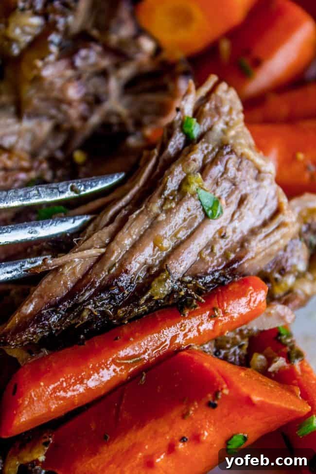 Easy Fall-Apart Pot Roast with Carrots (Slow Cooker) from The Food Charlatan. Super tender, juicy, fall-apart crock pot roast is not as hard as you think! This slow cooker recipe uses a few simple ingredients (one of them is patience) to make the most flavorful pot roast ever! #potroast #slowcooker #crockpot #roast #chuckroast #tender #juicy pot roast with carrots, mashed potatoes, and gravy. A close-up shot of a plate brimming with succulent pot roast, rich gravy, and vibrant carrots, perfectly paired with fluffy mashed potatoes. The textures and colors highlight a truly comforting and satisfying meal.