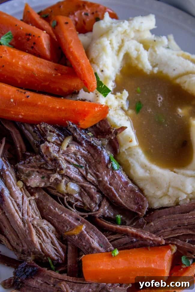 Easy Fall-Apart Pot Roast with Carrots (Slow Cooker) from The Food Charlatan. Super tender, juicy, fall-apart crock pot roast is not as hard as you think! This slow cooker recipe uses a few simple ingredients (one of them is patience) to make the most flavorful pot roast ever! #potroast #slowcooker #crockpot #roast #chuckroast #tender #juicy Roast meat and carrots with mashed potatoes and gravy. A beautifully plated pot roast meal, showcasing the tender beef and vibrant carrots, generously drizzled with rich gravy, and accompanied by a side of fluffy mashed potatoes, ready to be enjoyed.