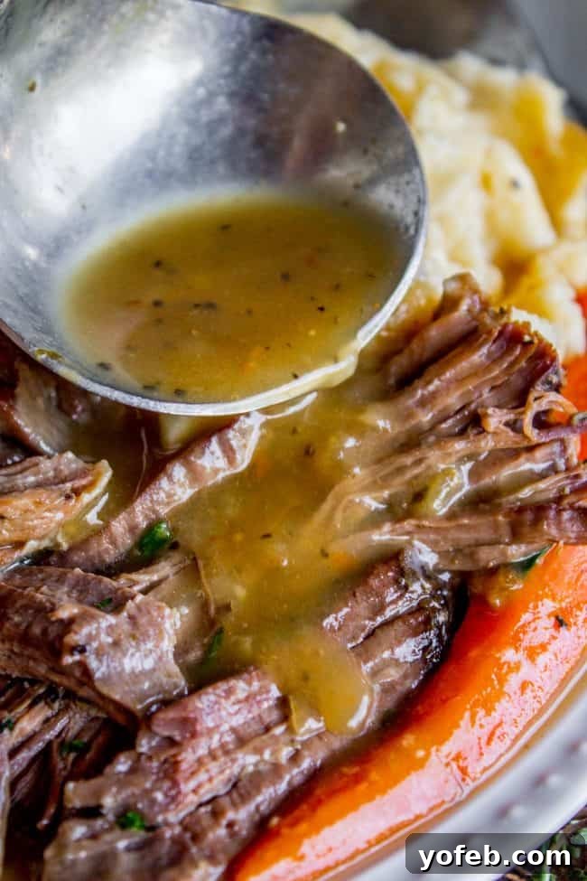 Easy Fall-Apart Pot Roast with Carrots (Slow Cooker) from The Food Charlatan. Super tender, juicy, fall-apart crock pot roast is not as hard as you think! This slow cooker recipe uses a few simple ingredients (one of them is patience) to make the most flavorful pot roast ever! #potroast #slowcooker #crockpot #roast #chuckroast #tender #juicy Pouring gravy over pot roast meat. A close-up shot of rich, homemade gravy being poured generously over a platter of shredded pot roast and tender carrots, enhancing the flavors and presentation of the dish.